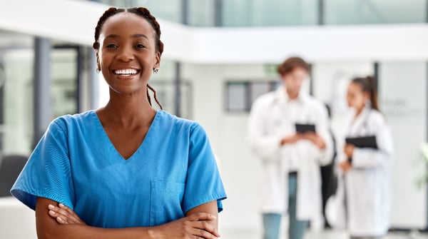 smiling black female in O-R scrubs with two females wearing lab coats in background crop