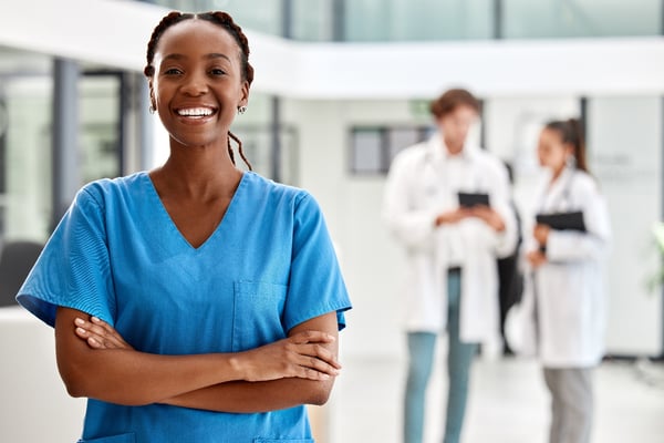 smiling black female in O-R scrubs with two females wearing lab coats in background