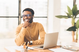 smiling black man sitting at work desk in front of laptop-1