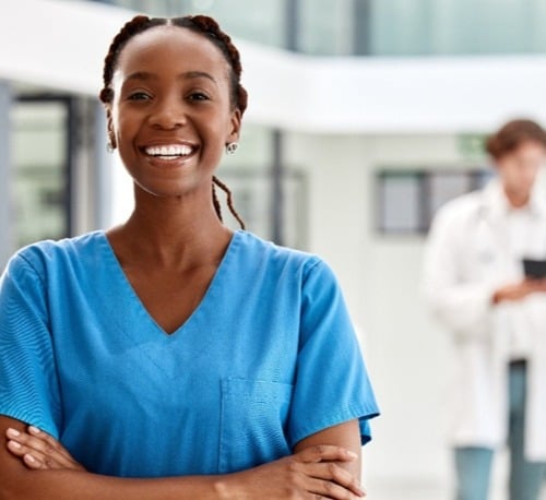 smiling black female in O-R scrubs with two females wearing lab coats in background-crop